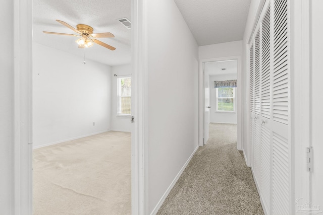 hallway with light colored carpet, plenty of natural light, and a textured ceiling