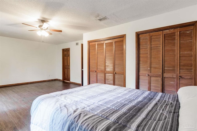 bedroom featuring visible vents, baseboards, two closets, and wood finished floors