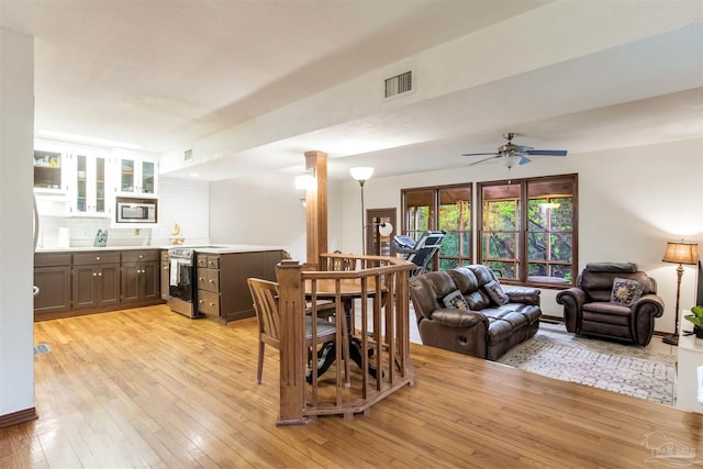 dining space with light wood-style floors, decorative columns, a ceiling fan, visible vents, and indoor bar