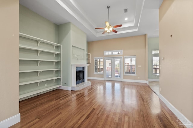 unfurnished living room with built in shelves, a raised ceiling, ceiling fan, and hardwood / wood-style floors