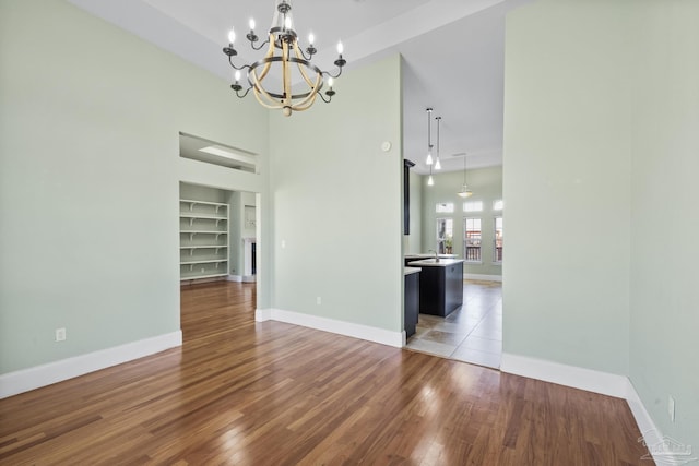 unfurnished dining area featuring built in shelves, hardwood / wood-style flooring, a notable chandelier, and a high ceiling