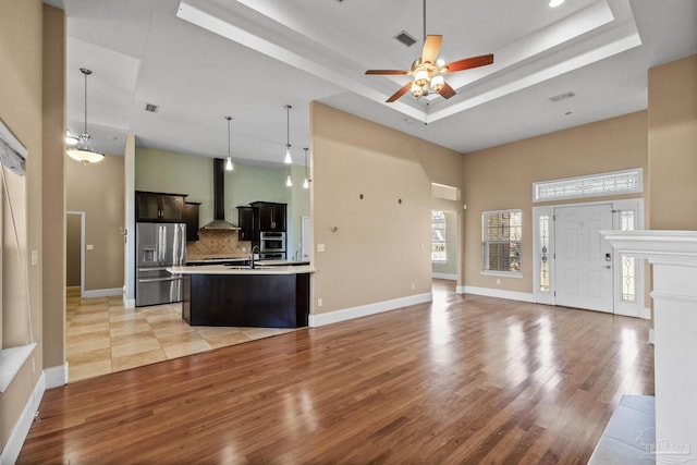 kitchen featuring appliances with stainless steel finishes, backsplash, a raised ceiling, a kitchen island with sink, and ceiling fan