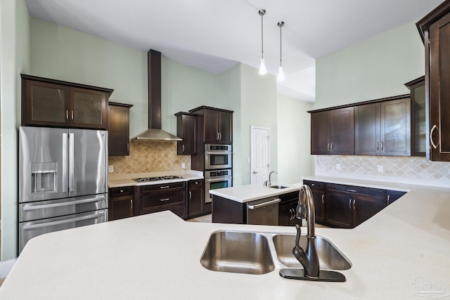 kitchen featuring dark brown cabinetry, wall chimney exhaust hood, hanging light fixtures, stainless steel appliances, and backsplash