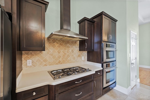 kitchen featuring light tile patterned flooring, backsplash, stainless steel appliances, and wall chimney range hood