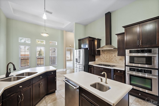 kitchen featuring a kitchen island with sink, wall chimney range hood, sink, and appliances with stainless steel finishes