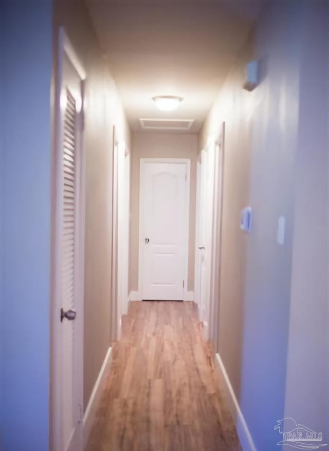 hallway with light wood-style flooring, visible vents, and baseboards