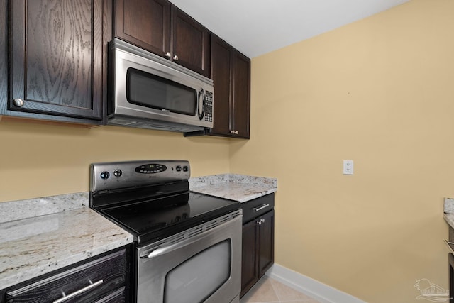 kitchen featuring light tile patterned floors, baseboards, light stone countertops, stainless steel appliances, and dark brown cabinets