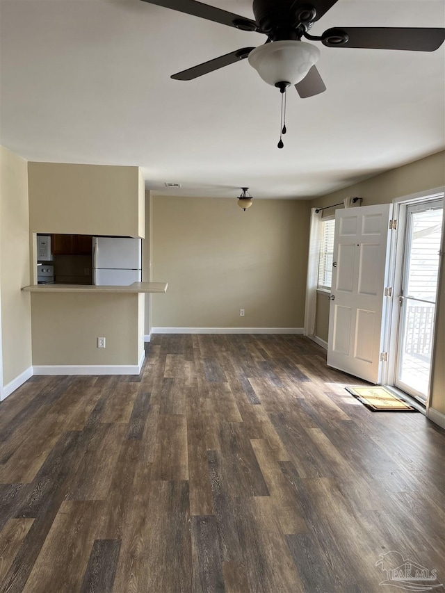 unfurnished living room with a healthy amount of sunlight, visible vents, baseboards, and dark wood-style flooring