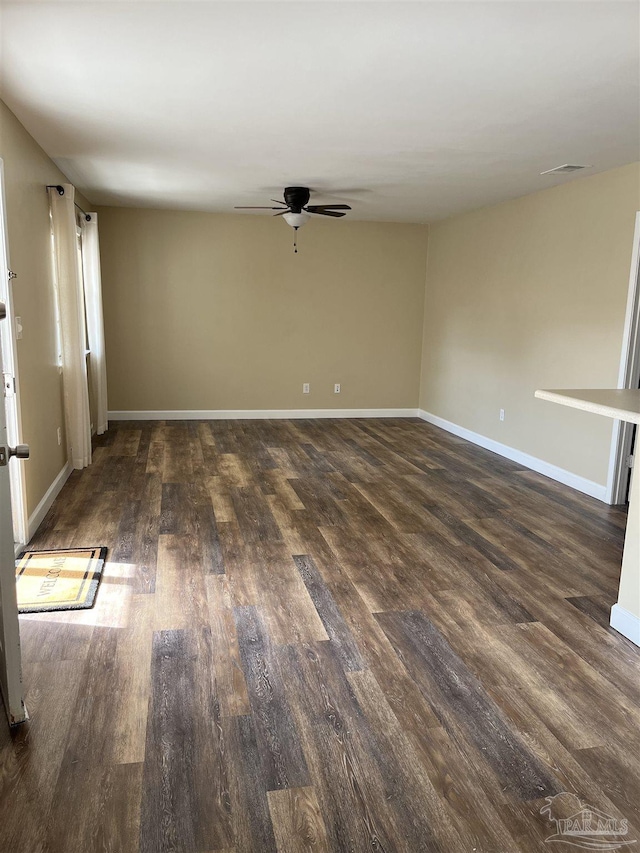 empty room featuring a ceiling fan, visible vents, dark wood finished floors, and baseboards