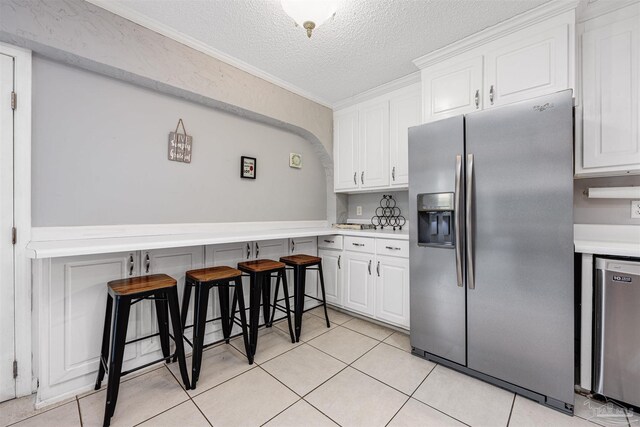 kitchen featuring light tile patterned flooring, a breakfast bar, a textured ceiling, white cabinets, and stainless steel appliances