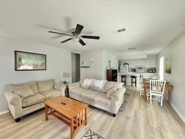 living area featuring a textured ceiling, light wood-type flooring, visible vents, and baseboards