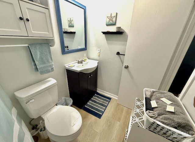 bathroom featuring toilet, baseboards, wood finished floors, and vanity