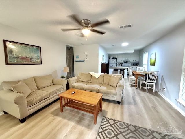 living room with baseboards, light wood-style flooring, visible vents, and a ceiling fan