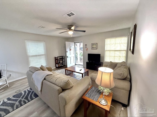 living area with a textured ceiling, light wood finished floors, visible vents, and baseboards