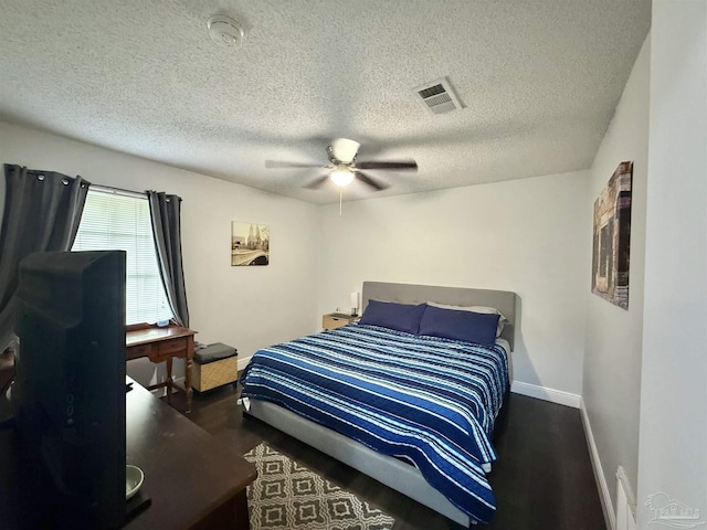 bedroom with a textured ceiling, dark wood-type flooring, visible vents, baseboards, and a ceiling fan