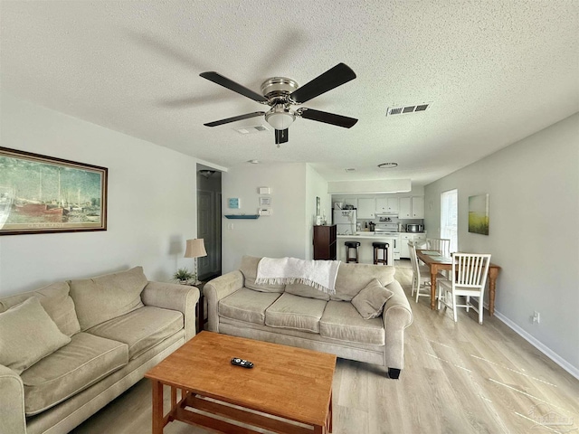 living room with a textured ceiling, baseboards, visible vents, and light wood-style floors