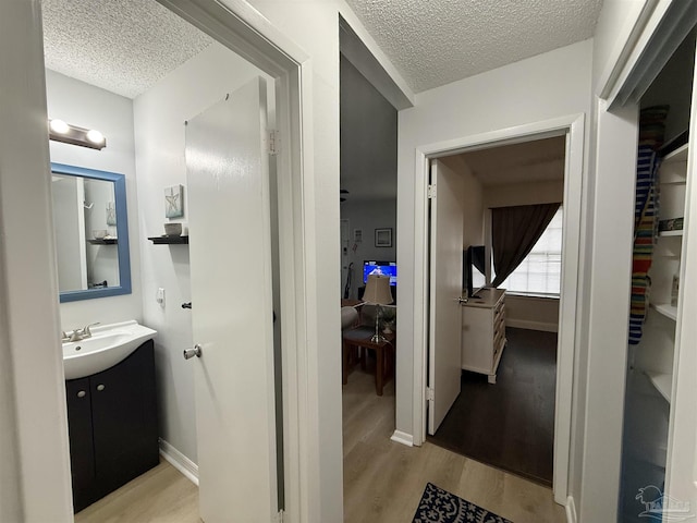 bathroom with a textured ceiling, wood finished floors, vanity, and baseboards