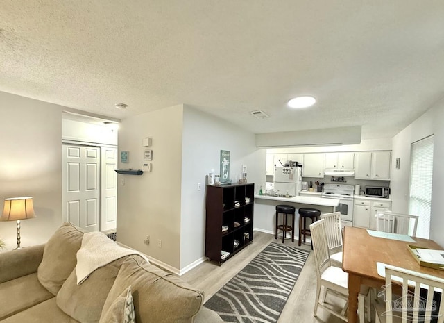 living area featuring light wood-type flooring, visible vents, a textured ceiling, and baseboards