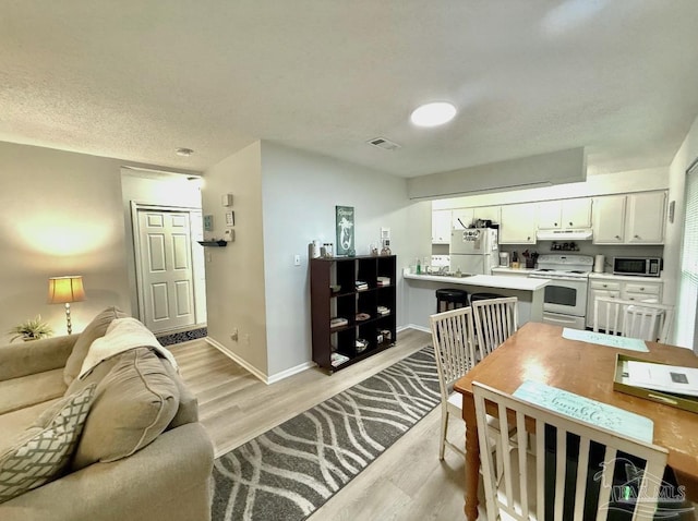 living area featuring light wood-style flooring, a textured ceiling, visible vents, and baseboards