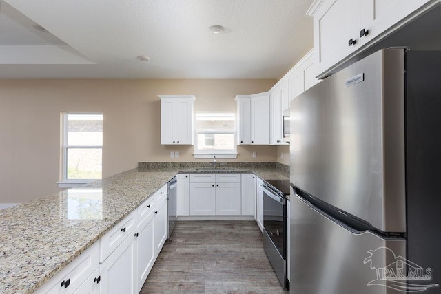 kitchen with stainless steel appliances, wood finished floors, a sink, white cabinets, and light stone countertops