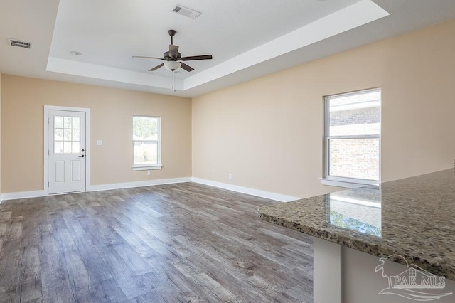 unfurnished living room featuring a tray ceiling, wood finished floors, visible vents, and baseboards