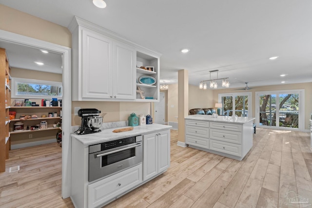 kitchen with light hardwood / wood-style flooring, decorative light fixtures, oven, white cabinetry, and ceiling fan