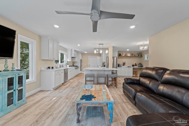 living room with ceiling fan with notable chandelier and light hardwood / wood-style floors