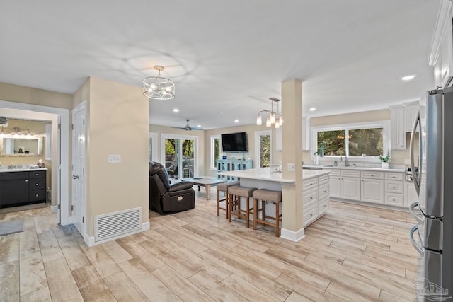 kitchen with white cabinetry, ceiling fan with notable chandelier, a breakfast bar area, stainless steel refrigerator, and a kitchen island