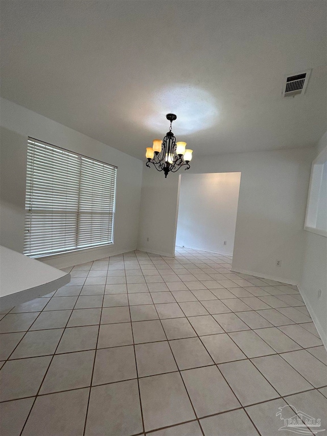 tiled empty room featuring an inviting chandelier