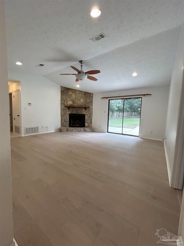 unfurnished living room featuring ceiling fan, a stone fireplace, a textured ceiling, and light hardwood / wood-style floors