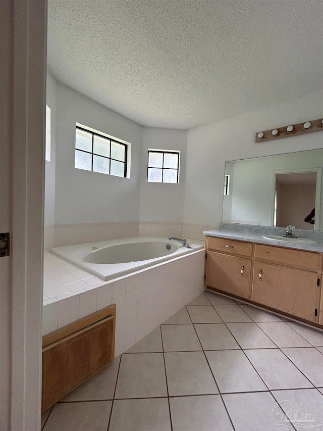 bathroom with tile patterned floors, a relaxing tiled tub, vanity, and a textured ceiling