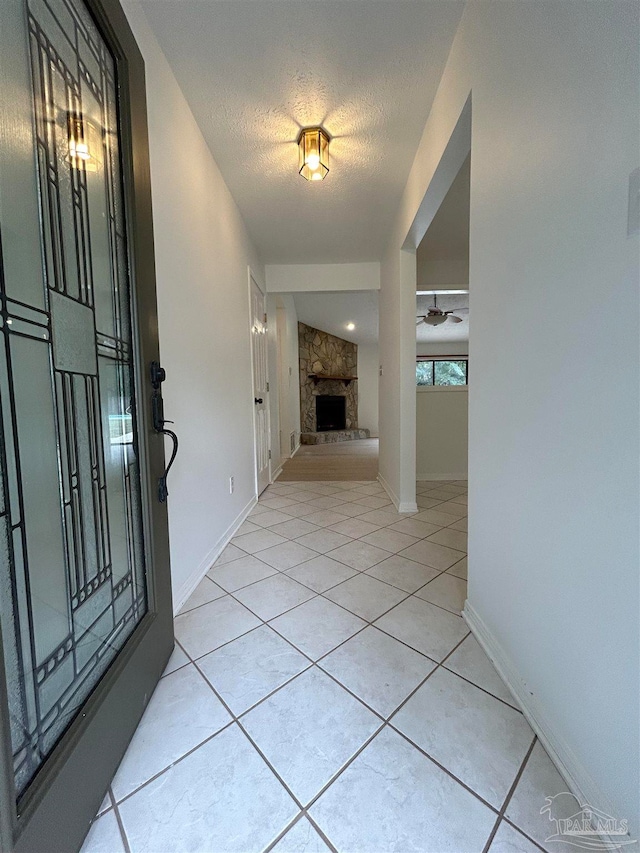 entryway with a stone fireplace, a textured ceiling, and light tile patterned floors