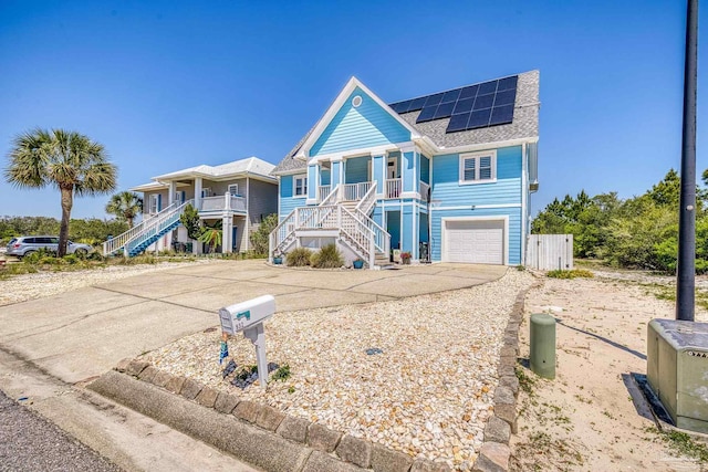 coastal inspired home featuring roof mounted solar panels, covered porch, concrete driveway, and stairway