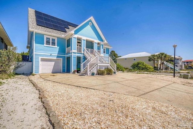 raised beach house featuring concrete driveway, stairs, a porch, solar panels, and a garage