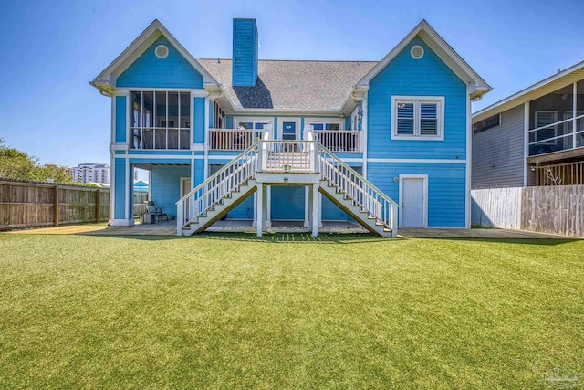 rear view of house with a sunroom, a lawn, a chimney, fence, and stairway