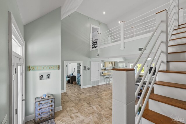 staircase with visible vents, baseboards, high vaulted ceiling, and plenty of natural light