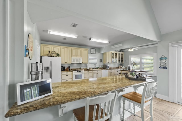 kitchen featuring cream cabinetry, a breakfast bar area, white appliances, and visible vents