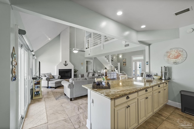 kitchen with a peninsula, a ceiling fan, visible vents, light stone counters, and cream cabinets