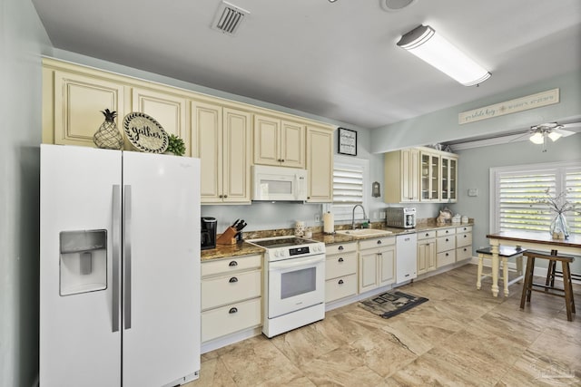 kitchen featuring a sink, cream cabinetry, white appliances, and light stone countertops