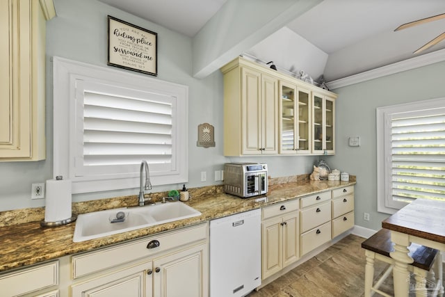 kitchen featuring glass insert cabinets, cream cabinetry, stone countertops, a sink, and white dishwasher