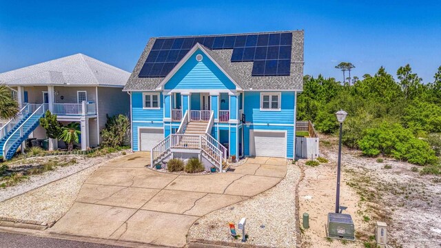coastal home with solar panels, a porch, a garage, stairway, and concrete driveway