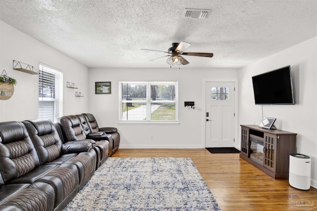 living area featuring visible vents, plenty of natural light, ceiling fan, and wood finished floors