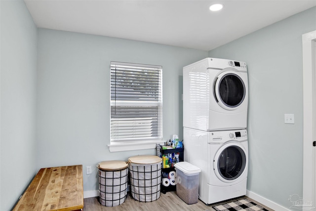 laundry room featuring laundry area, stacked washing maching and dryer, baseboards, and wood finished floors