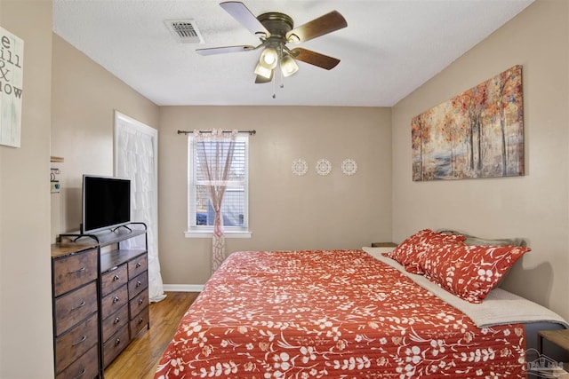 bedroom featuring light wood finished floors, visible vents, baseboards, a textured ceiling, and a ceiling fan