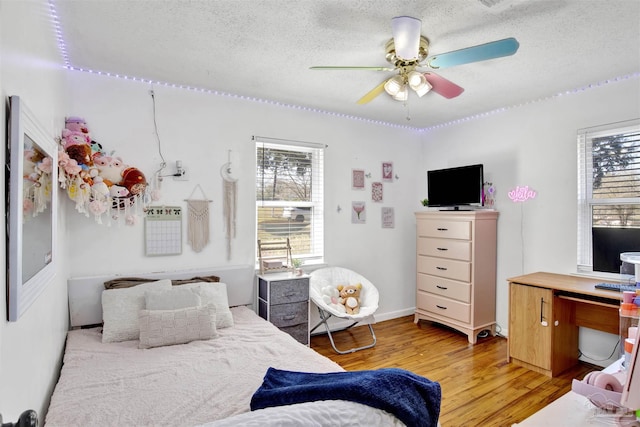 bedroom featuring multiple windows, a textured ceiling, light wood-type flooring, and ceiling fan