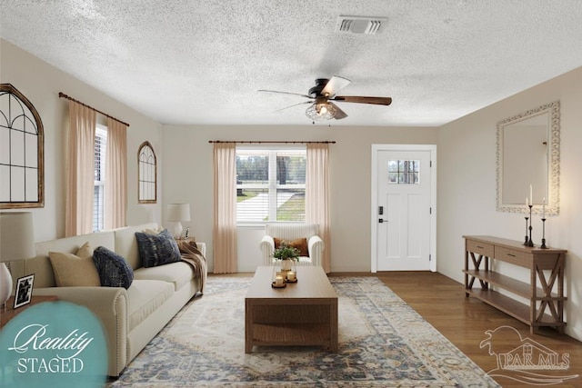 living room with a textured ceiling, wood finished floors, visible vents, and ceiling fan