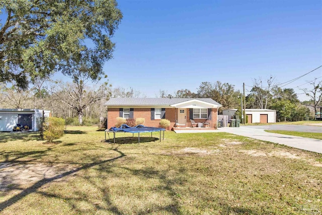 view of front of property with brick siding, a detached garage, a trampoline, a front yard, and an outbuilding