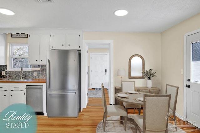 kitchen featuring decorative backsplash, appliances with stainless steel finishes, light wood-style floors, white cabinetry, and a sink