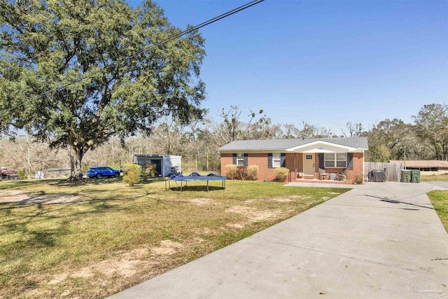 view of front facade with brick siding, a front lawn, a trampoline, fence, and driveway