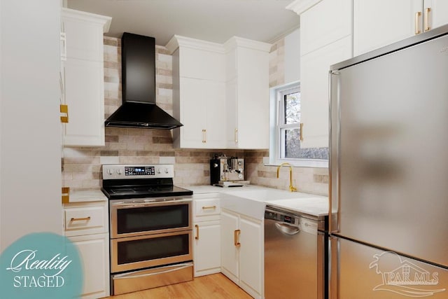 kitchen featuring tasteful backsplash, wall chimney range hood, light countertops, appliances with stainless steel finishes, and a sink